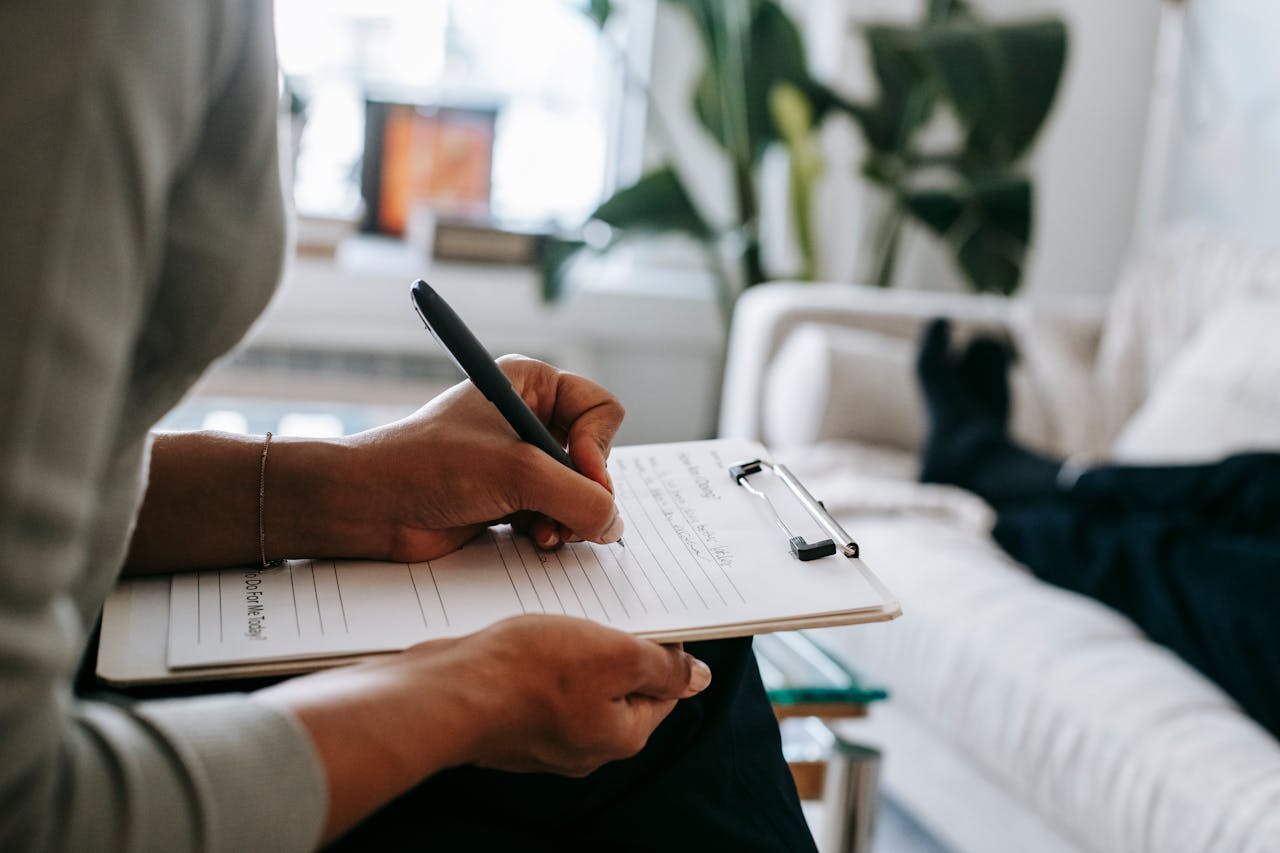 hero-img-02 Unrecognizable ethnic female therapist taking notes on clipboard while filling out form during psychological appointment with anonymous client lying on blurred background