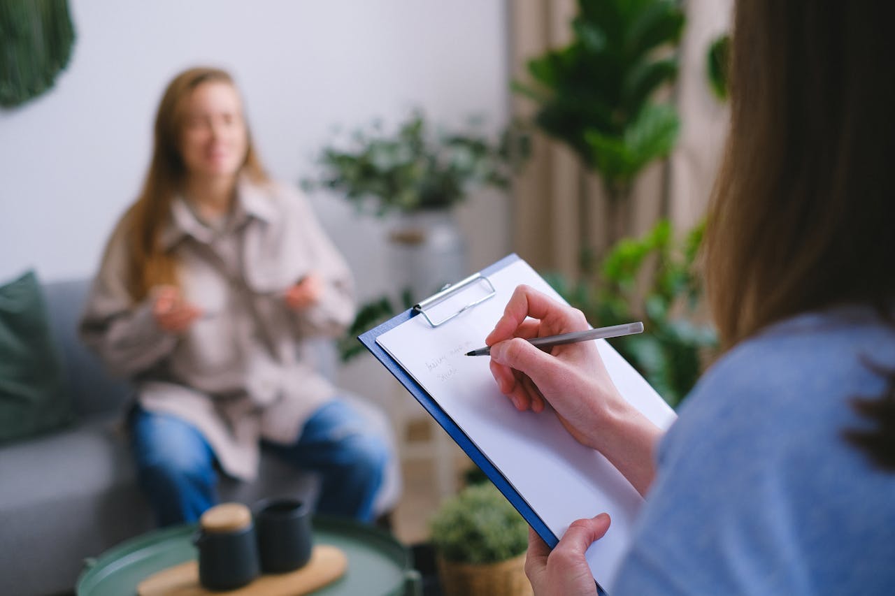 gallery-2 Unrecognizable professional female psychologist writing on clipboard while sitting against client on blurred background during psychotherapy session in light office