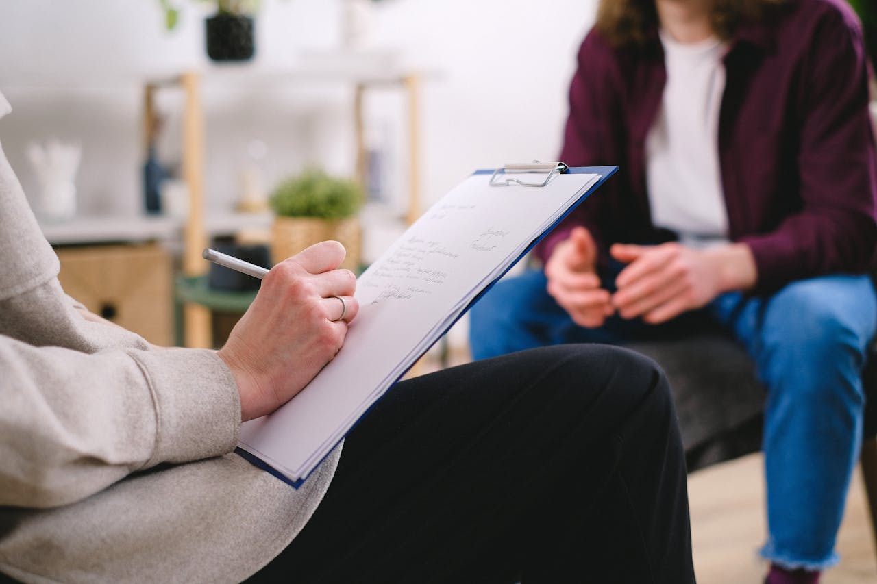 gallery-6 Close-up of a therapist writing notes on a clipboard while conversing with a patient.